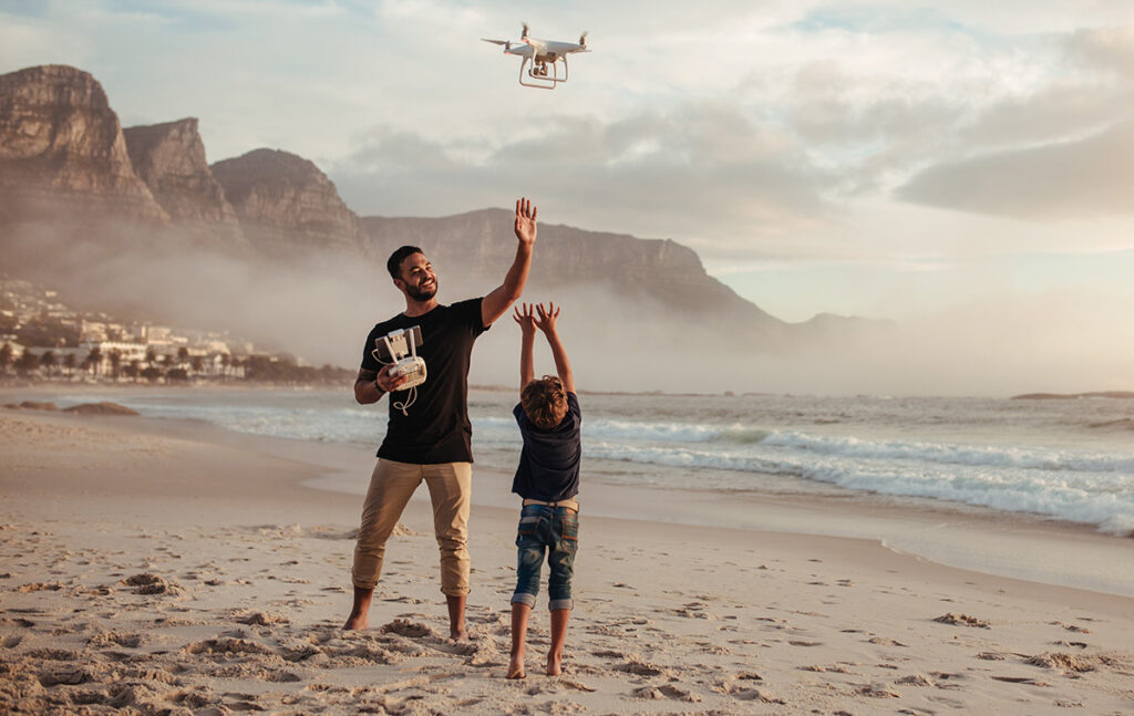 Father and son flying drone with remote control at beach